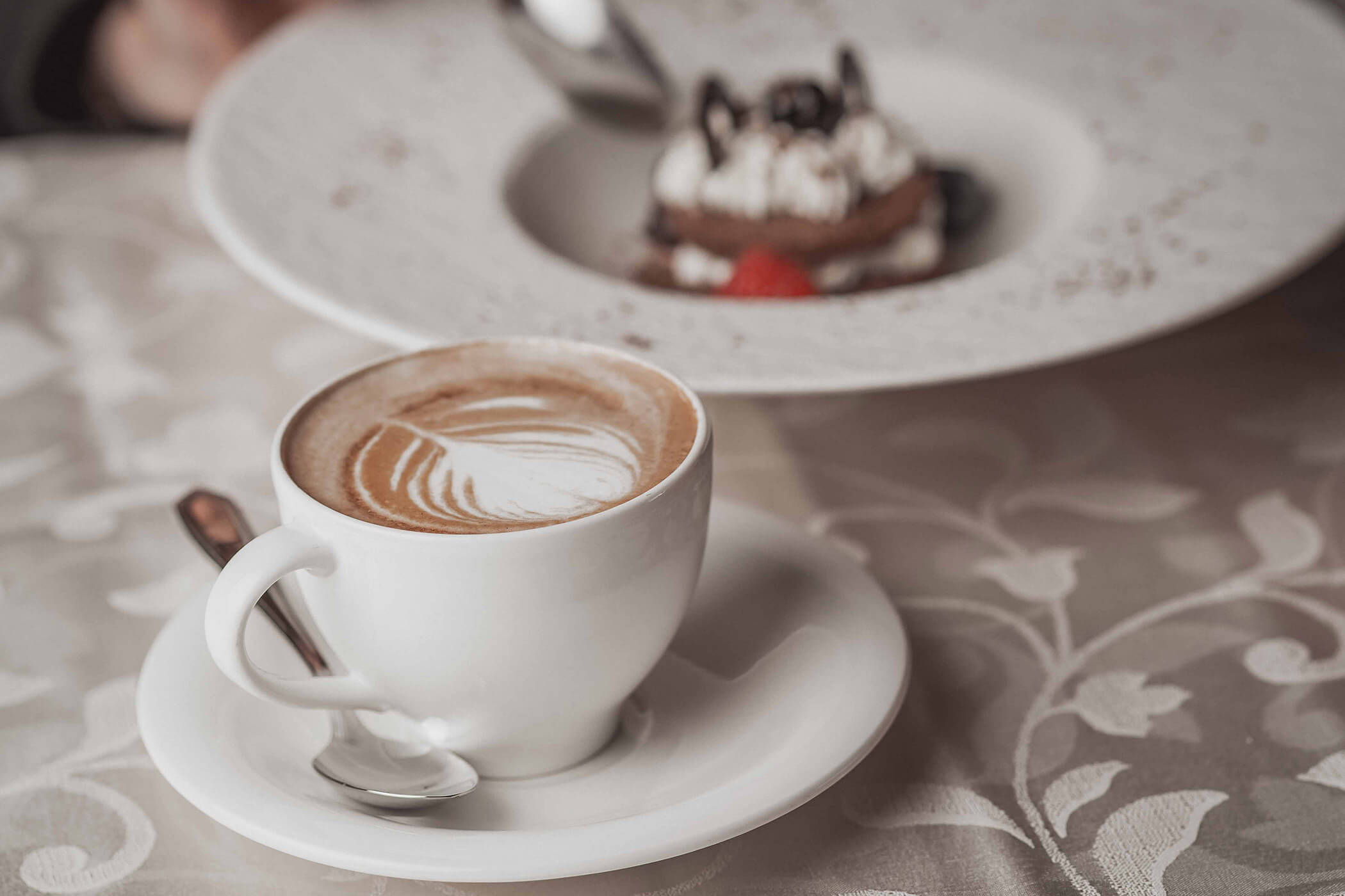 Cappucchino at the table with dessert in the background - Hotel Continental