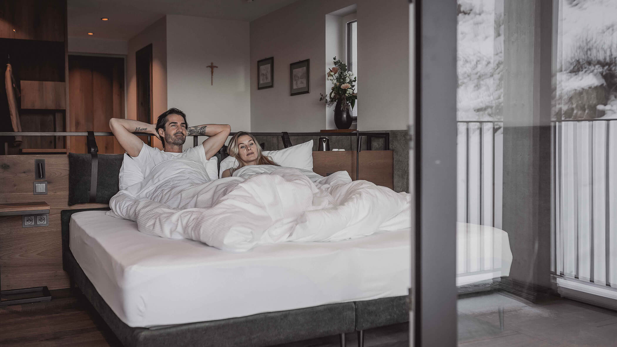 Ein Paar liegt im Doppelbett und schaut nach draußen - Hotel Continental