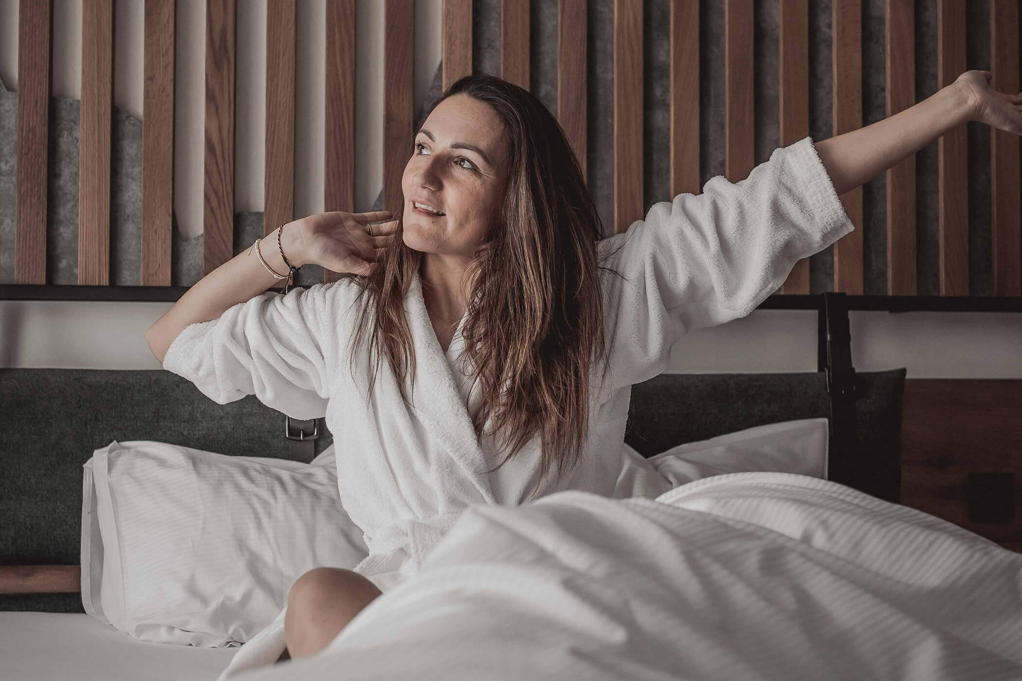 Woman in bathrobe stretches in bed - Hotel Continental