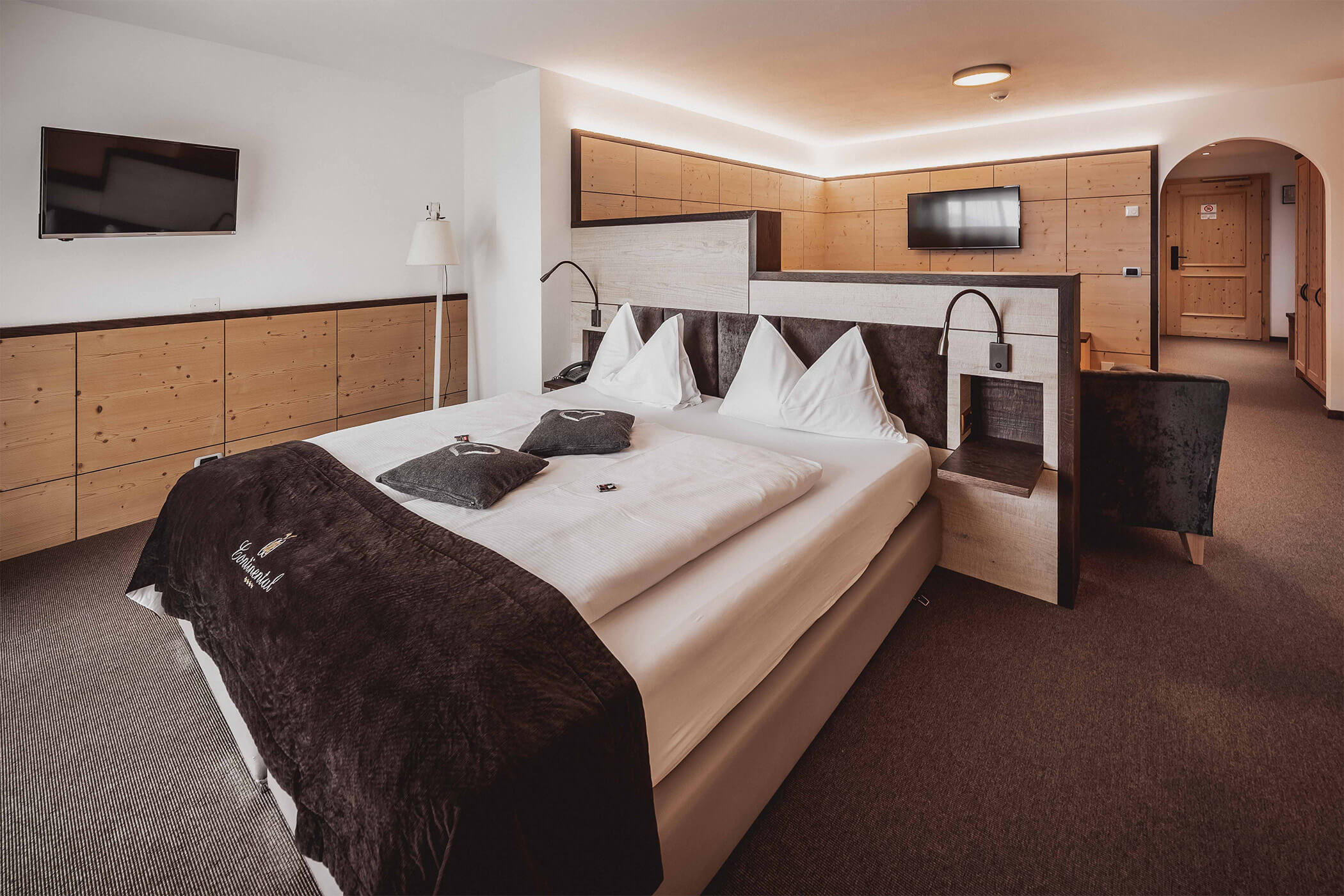 Double bed with light-coloured carpet and TV and seating area in the Classic Junior Suite 
