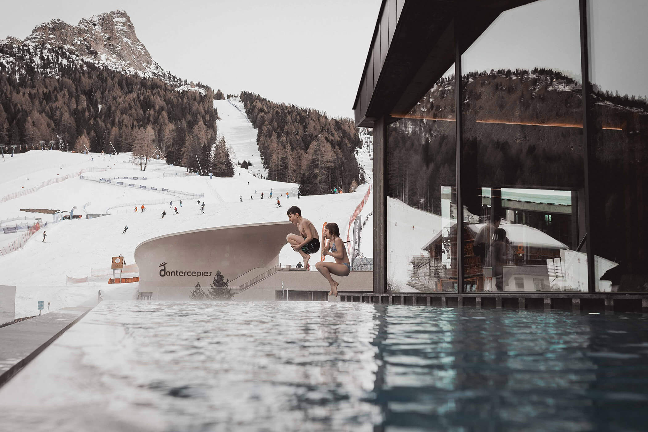 Two children jumping into the pool, in the background various skiers on the Sella Ronda - Hotel Continental