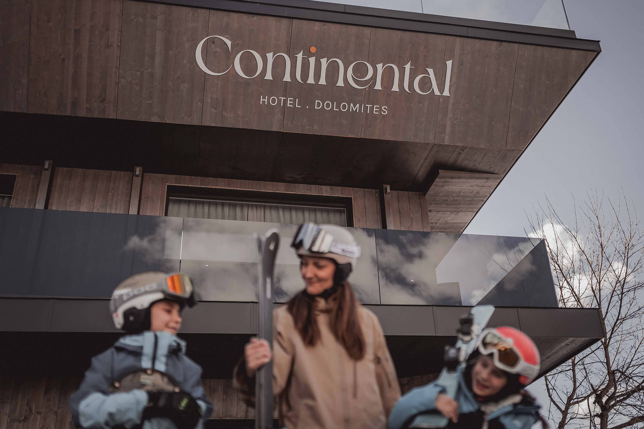 Two children and a woman with ski equipment in front of the Hotel Continental