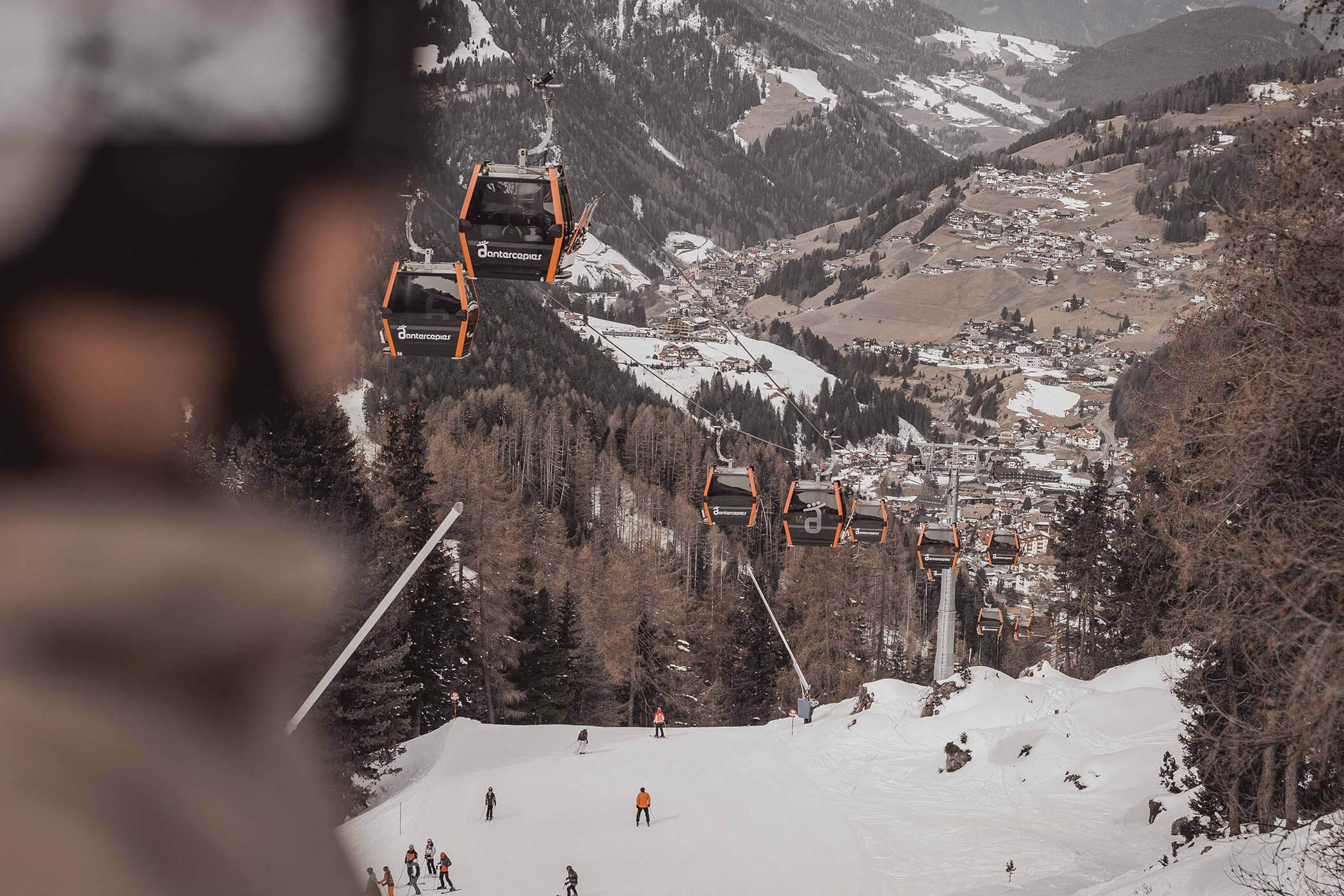 A skier looks out over the Sella Ronda slopes, with the gondolas above him - Hotel Continental
